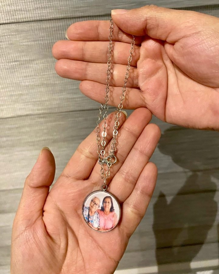 Un dije redondo con la foto de una señora y su mamá, sostenido en la palma de la mano junto a su cadena de plata.