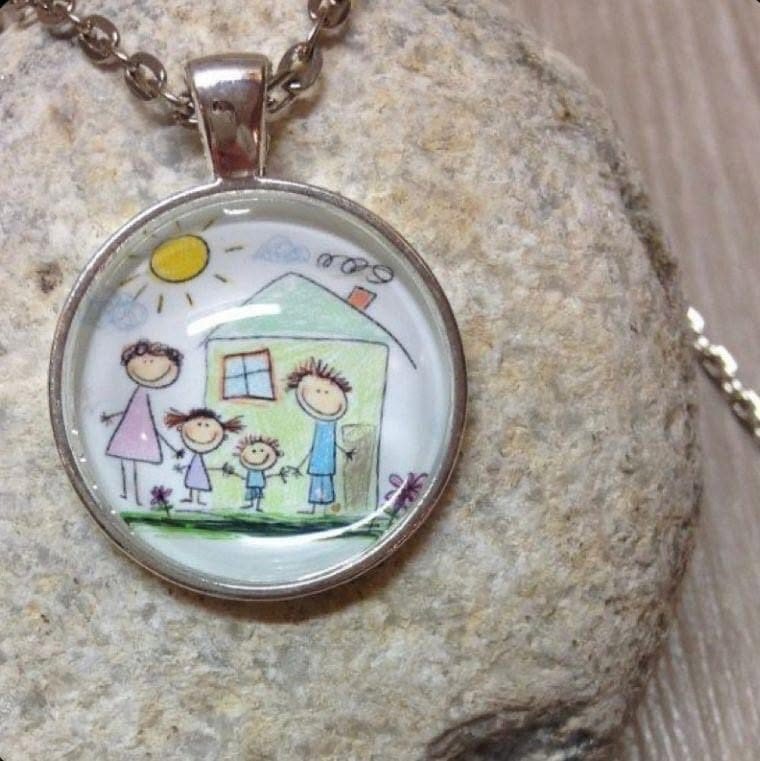 Dije con el dibujo de una casa, un sol y una familia de cuatro tomada de la mano afuera.