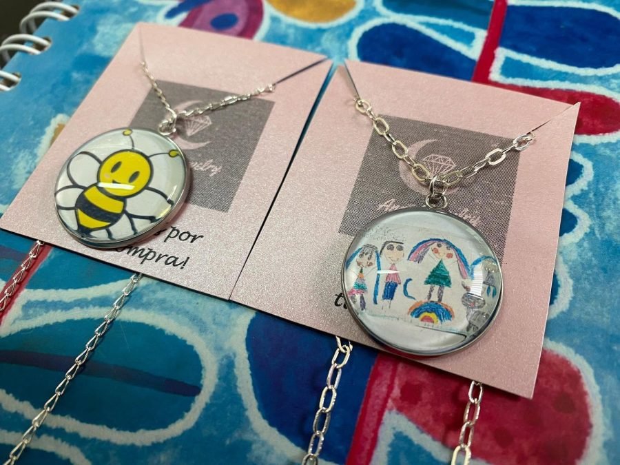 Dos collares sobre tarjetas rosas: uno con una abeja de caricatura y otro con un dibujo familiar con arcoíris.